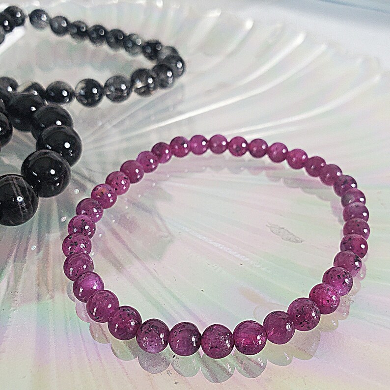 May include: A pink gemstone bracelet with round beads. The bracelet is made of small, round beads that are strung together on a clear elastic cord.