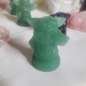 May include: A green figurine of a character from the Star Wars franchise. The figurine is made of a translucent material and has a detailed design.