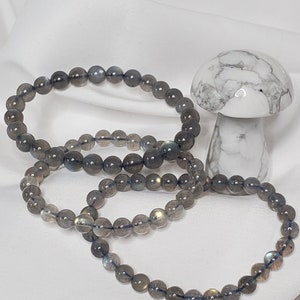 May include: Three gray labradorite gemstone bracelets with a white howlite mushroom in the background.