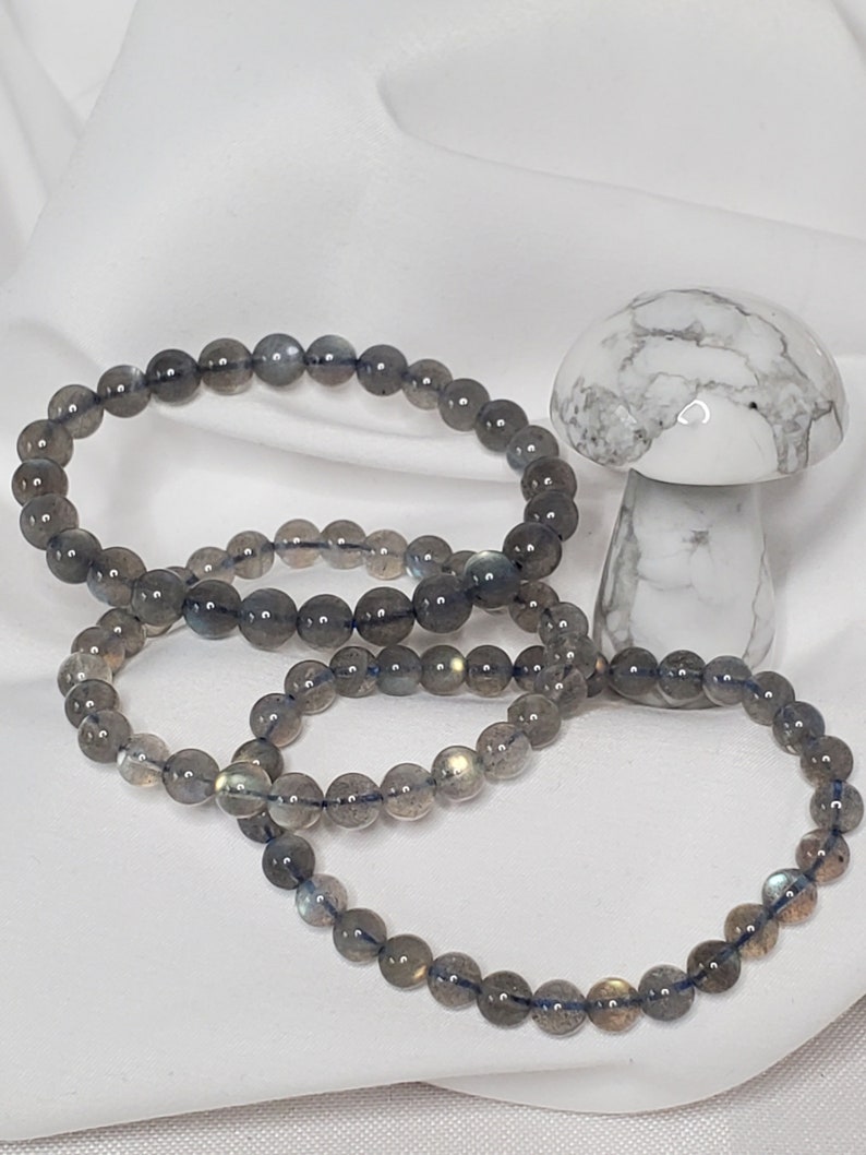 May include: Three gray labradorite gemstone bracelets with a white howlite mushroom in the background.
