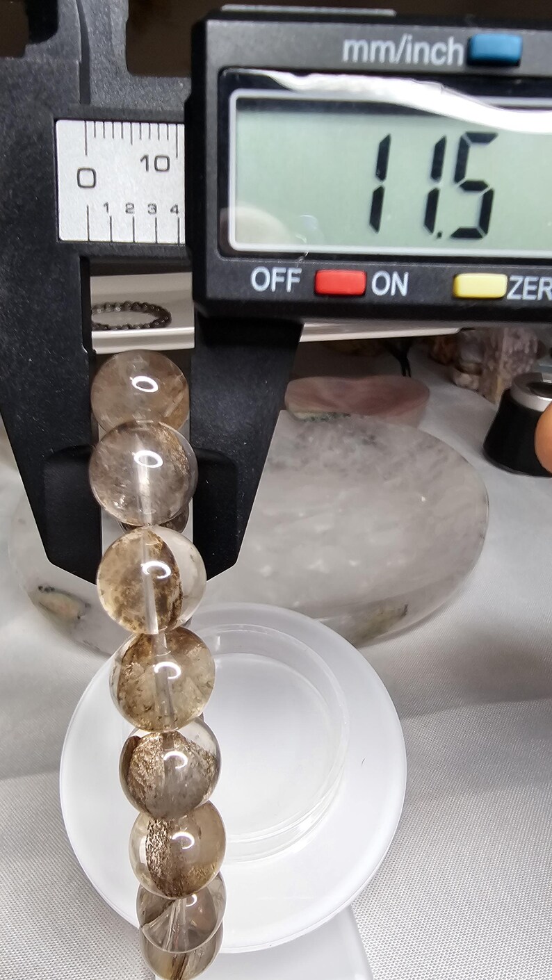 May include: A close-up of a brown and clear crystal bead bracelet being measured with a digital caliper. The caliper reads 1.15 inches.