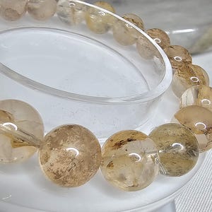 May include: A bracelet made of round, translucent, light brown beads with gold flecks. The beads are strung together on a clear elastic cord.