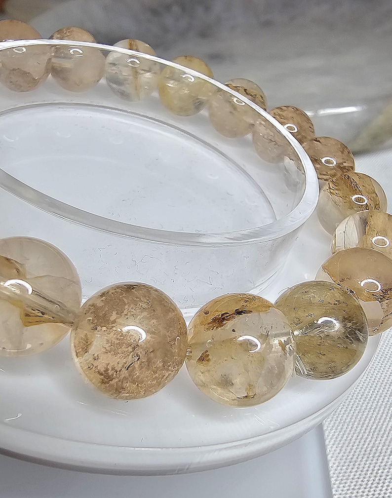 May include: A bracelet made of round, translucent, light brown beads with gold flecks. The beads are strung together on a clear elastic cord.