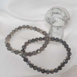 May include: Two gray labradorite gemstone bracelets with a white mushroom figurine in the background.