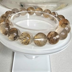 May include: A bracelet made of brown and clear crystal beads with a cloudy, speckled appearance. The beads are round and have a smooth, polished finish.