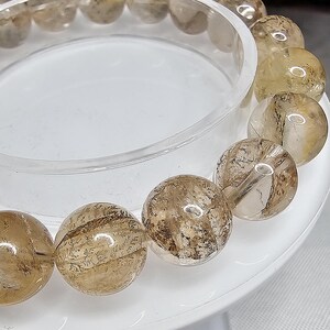 May include: A bracelet made of clear quartz beads with brown inclusions. The beads are round and have a smooth, polished finish.