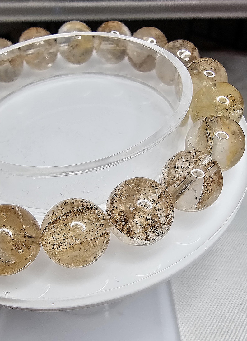 May include: A bracelet made of clear quartz beads with brown inclusions. The beads are round and have a smooth, polished finish.