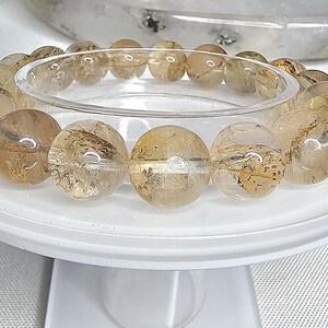 May include: A bracelet made of round, translucent, light brown and gold beads with a clear, glassy finish. The beads are arranged in a circle and are strung on a clear elastic cord.