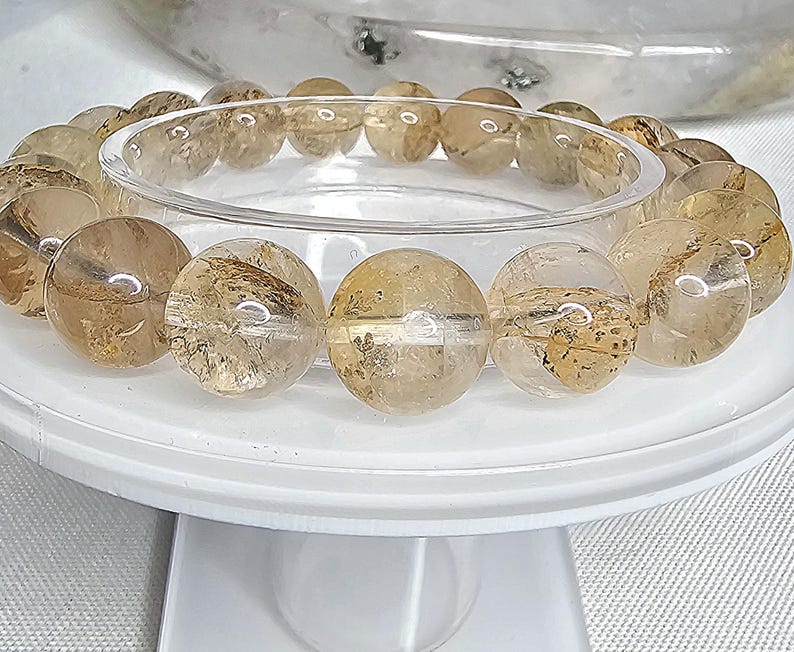May include: A bracelet made of round, translucent, light brown and gold beads with a clear, glassy finish. The beads are arranged in a circle and are strung on a clear elastic cord.