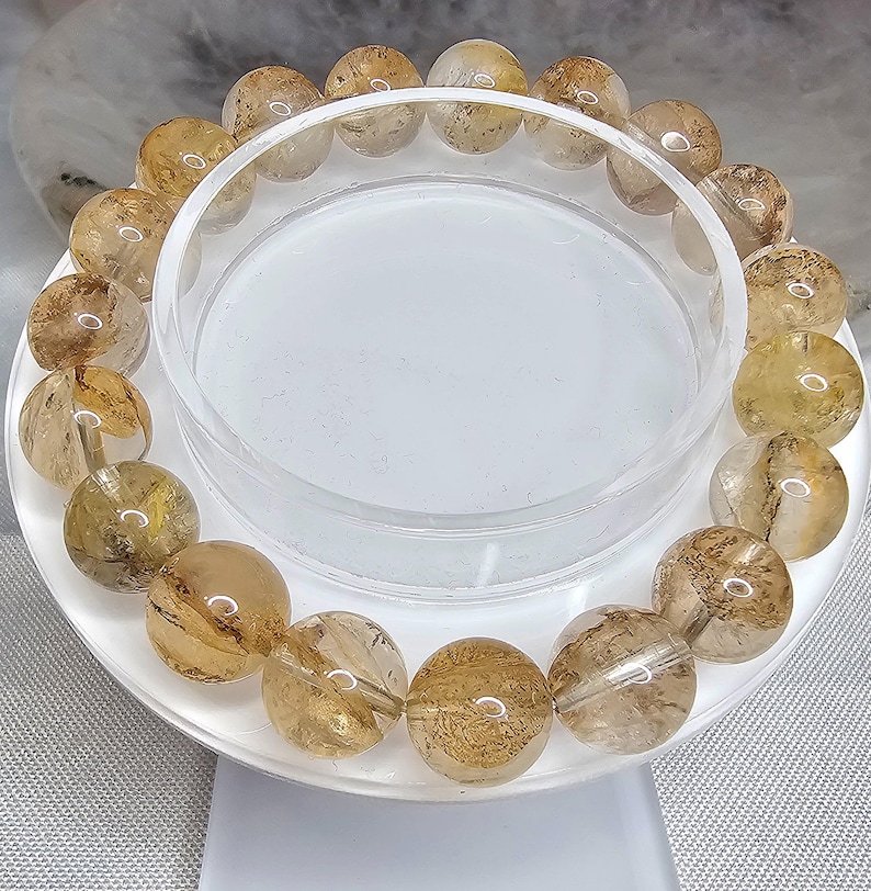May include: A bracelet made of golden brown, translucent, round beads with a light brown, cloudy, marbled pattern. The beads are strung together on a clear elastic cord.