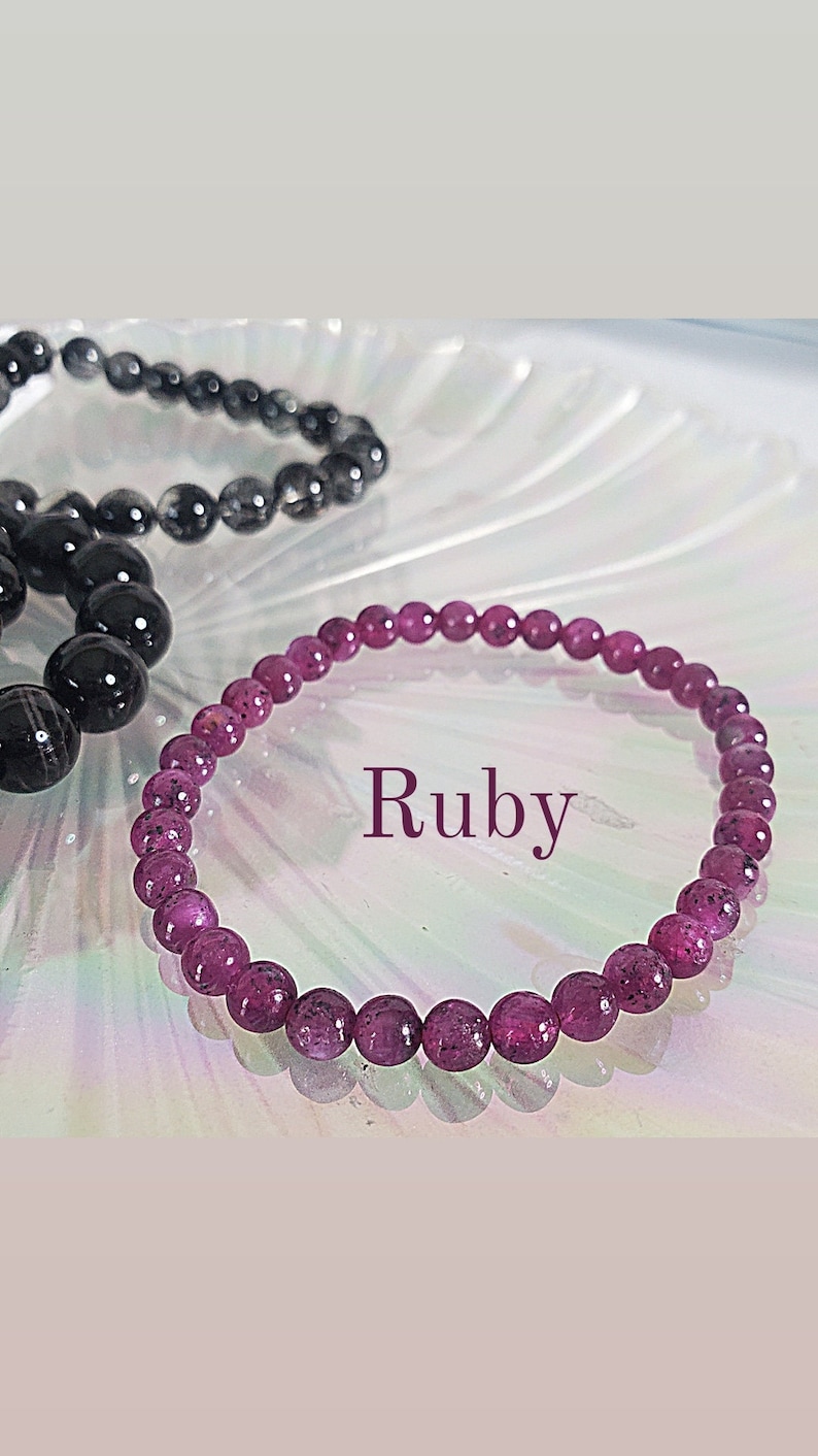 May include: A red ruby gemstone bracelet with round beads. The bracelet is on a white background with the word "Ruby" written in black.