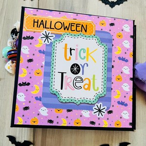 May include: A Halloween-themed scrapbook with a purple background featuring ghosts, pumpkins, moons, and spiders. The cover has the word "HALLOWEEN" in orange and a central label that says "trick or treat". Decorative bats and a spider web are also present.