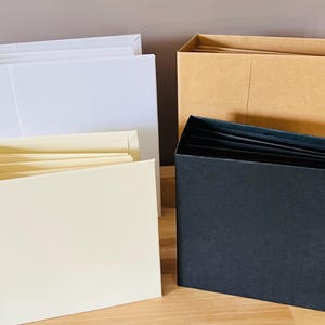May include: Three accordion style photo albums, one white, one cream, and one black.