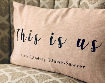 May include: A pink throw pillow with the text "This is us" and the names "Cam, Lindsey, Eloise, Sawyer" printed in black.