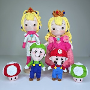 Op de afbeelding: Een set van vijf gehaakte pluche speelgoedfiguren met personages uit de Super Mario-franchise. De set bevat Prinses Peach, Prinses Daisy, Mario, Luigi en twee paddenstoelfiguren.