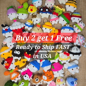 Op de afbeelding: Een verzameling kleurrijke, gehaakte sleutelhangers in verschillende dieren- en voedselontwerpen. De sleutelhangers hebben een verscheidenheid aan kleuren, waaronder rood, blauw, geel en groen. De tekst "Buy 2 get 1 Free" en "Ready to Ship FAST in USA" is zichtbaar.