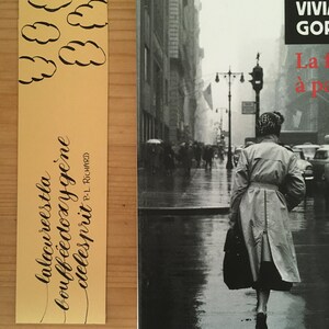 May include: A yellow bookmark featuring black hand-drawn clouds and the text "la lecure est la bouff&eacute;e d'oxyg&egrave;ne de l'esprit" by P.-L. Richard, placed next to a book cover showing a black and white photograph of a person in a trench coat on a city street.