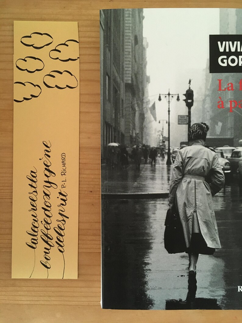 May include: A yellow bookmark featuring black hand-drawn clouds and the text "la lecure est la bouff&eacute;e d'oxyg&egrave;ne de l'esprit" by P.-L. Richard, placed next to a book cover showing a black and white photograph of a person in a trench coat on a city street.
