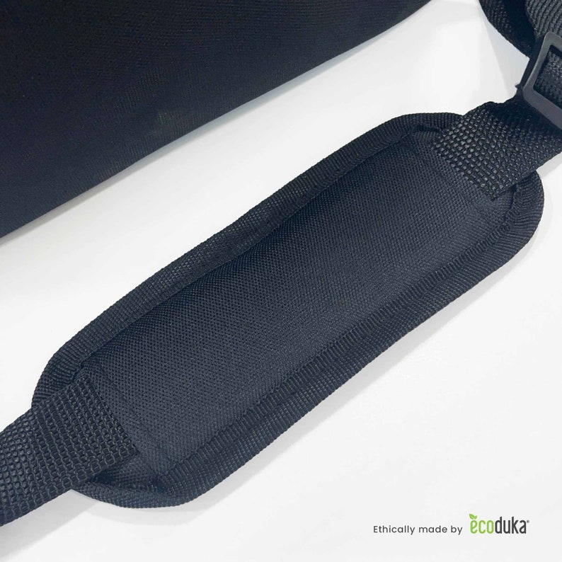 May include: Close-up of a black shoulder strap with a padded section for comfort. The strap is made of a durable, textured fabric and features a black plastic buckle. The image is set against a white background.