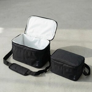 May include: Two black insulated lunch bags. One bag is open, revealing a white interior, and the other is closed. Both bags have a black shoulder strap and a small white logo on the front.