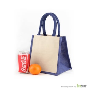 May include: A beige and blue tote bag with a Coca-Cola can and an orange. The bag has a rectangular shape with blue trim and handles. The Coca-Cola can is red and white, and the orange is round and orange.