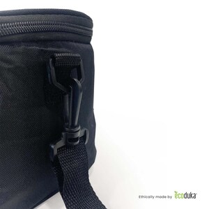 May include: Close-up of a black insulated bag with a zipper closure and a detachable shoulder strap. The bag features a black plastic clip and a woven strap. The bag is set against a white background.