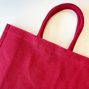 May include: A red jute tote bag with thick, red rope handles.