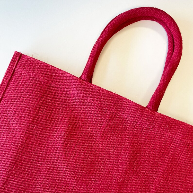 May include: A red jute tote bag with thick, red rope handles.