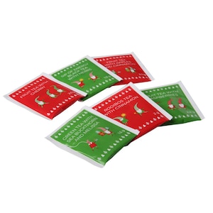 May include: Six different tea bags with festive Christmas designs. The tea bags are red and green with a gnome illustration and text describing the tea flavor. The flavors are: Fruit Tea with Cherry, Sip of Energy Black Tea with Herbs, Green Tea with Sea Buckthorn and Melissa, Rooibos Tea with Cinnamon, Fruit Tea with Apples and Cinnamon, and Fruit Tea with Raspberries.