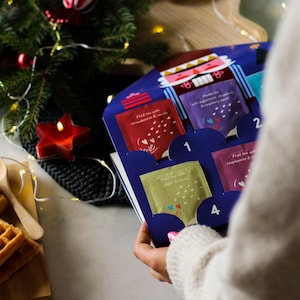 May include: A blue and white advent calendar with a nutcracker design. The calendar has four visible tea bags with different flavors: Fruit tea with strawberries & vanilla, Herbal tea with peppermint, chamomile & raspberry, Fruit tea with raspberries & lemon, and Fruit tea with pepper & lemon. The calendar is open to reveal the tea bags.