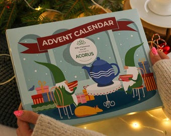 Könnte beinhalten: Eine blaue und weiße Adventskalender-Box mit dem Text "Advent Calendar" und "Elfin Christmas Tea Set" auf der Vorderseite. Die Box zeigt eine skurrile Illustration von zwei Wichteln, die an einem Tisch mit einer Teekanne und Tassen sitzen.