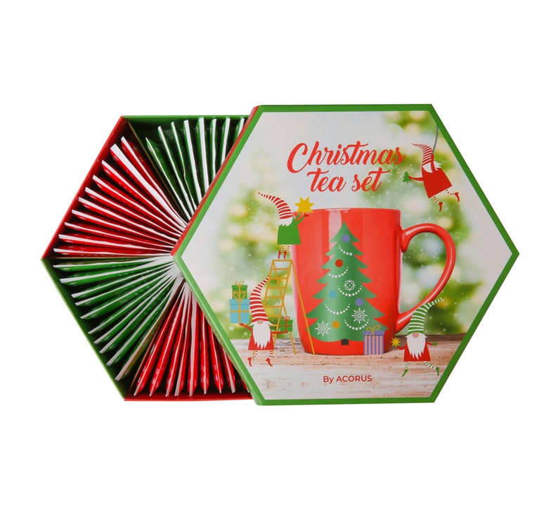 May include: A hexagonal box with a red and green Christmas tea set. The box features a red mug with a Christmas tree design and the text "Christmas tea set" and "By ACORUS".