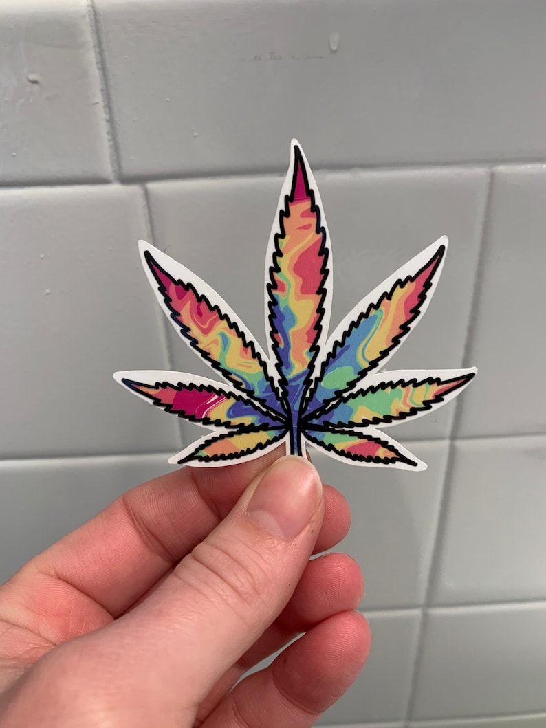 K&ouml;nnte beinhalten: Ein bunter Batik-Cannabisblatt-Aufkleber mit schwarzem Umriss.