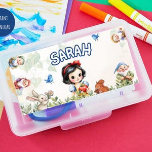 Pu&ograve; includere: Un astuccio trasparente in plastica con un'illustrazione colorata di Biancaneve e il nome "Sarah". L'illustrazione include Biancaneve, nani, un coniglio e un uccellino blu. L'astuccio &egrave; su una superficie rossa con pennarelli.