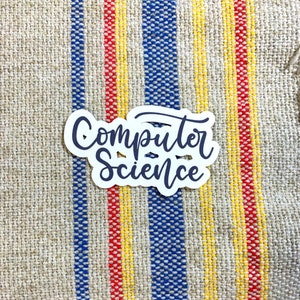 May include: White sticker with the text "Computer Science" written in black cursive lettering on a striped fabric background.