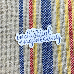 May include: A white sticker with the words "industrial engineering" written in purple cursive lettering on a striped fabric background.