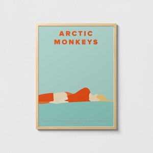 May include: A framed poster with a teal background and the text "ARCTIC MONKEYS" in orange. A stylized illustration of a person lying on their side in orange and white is at the bottom of the poster.