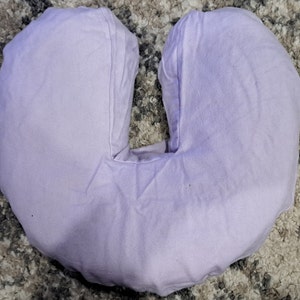 May include: A lavender-colored U-shaped pillow for neck support. The pillow is made of soft fabric and is designed to provide comfort and support for the neck and shoulders.