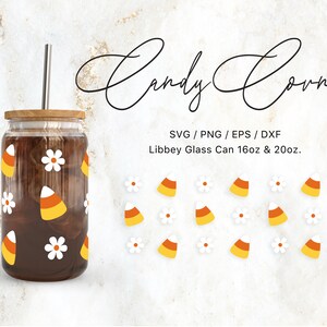 Puede incluir: Una lata de vidrio con un líquido marrón y una pajita. La lata está decorada con margaritas blancas y maíz dulce naranja y amarillo. El texto "Candy Corn" está escrito en cursiva sobre la lata. El texto "SVG/PNG/EPS/DXF" y "Libbey Glass Can 16oz & 20oz." está escrito debajo de la lata. Hay imágenes adicionales de maíz dulce y margaritas alrededor de la lata.