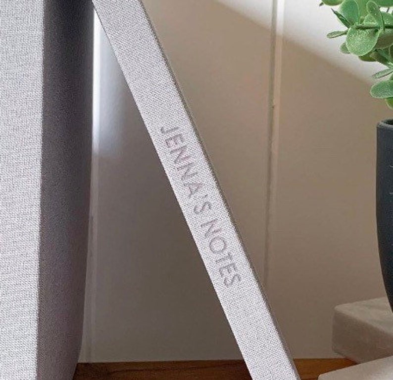 May include: A gray linen-covered notebook with the text "Jenna's Notes" embossed on the spine.