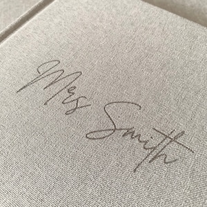 May include: A close-up of a light gray fabric journal with the name "Mrs. Smith" written in cursive on the front cover.