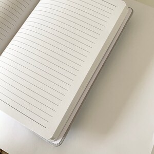 May include: A white notebook with lined pages, open to reveal the blank pages. The notebook is closed and the spine is visible.