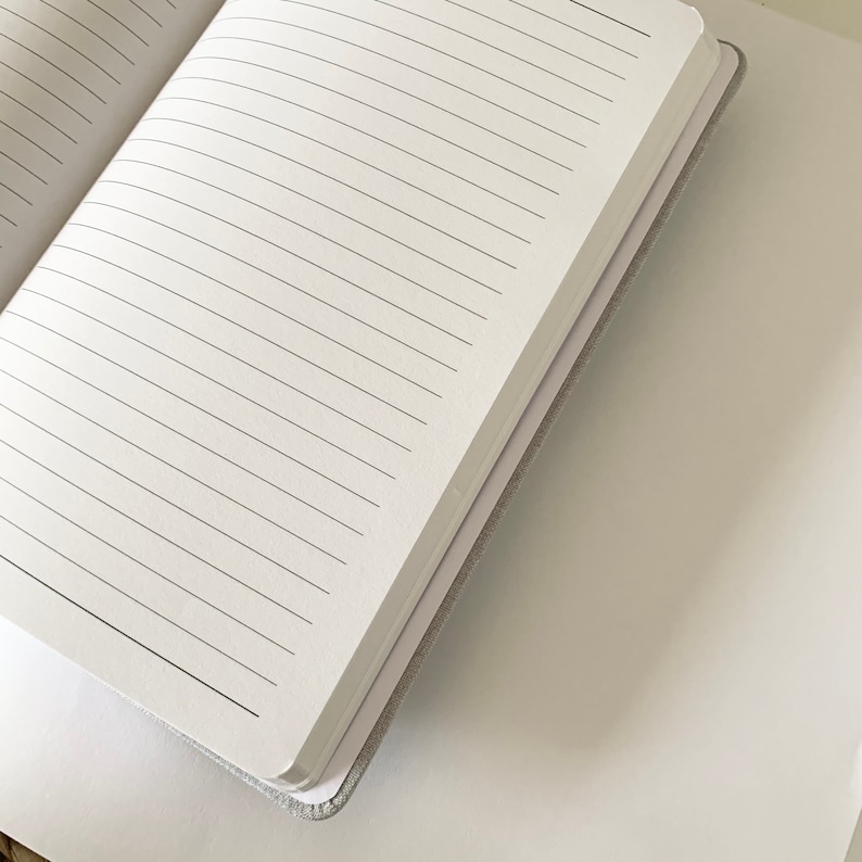May include: A white notebook with lined pages, open to reveal the blank pages. The notebook is closed and the spine is visible.
