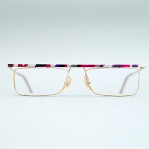 May include: Gold-rimmed glasses with a colorful, abstract pattern on the bridge.