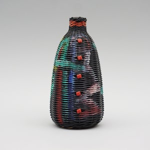 May include: A black woven bottle with colourful stripes and red buttons. The bottle is a decorative piece and is made of natural materials.