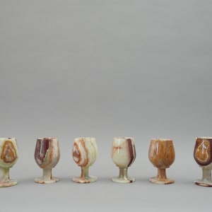 Może przedstawiać: Zestaw sześciu małych, przezroczystych kieliszków na nóżce wykonanych z onyksu. Kieliszki mają unikalny, marmurowy wzór w odcieniach brązu, bieli i zieleni.