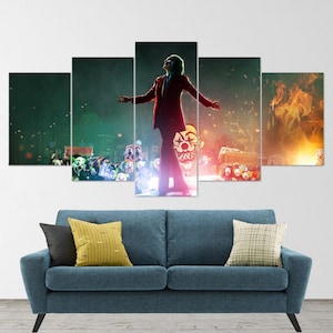 May include: A five-piece canvas print set featuring a red-clad Joker character from the movie "Joker" standing in front of a crowd of people wearing clown masks. The background is a dark cityscape with flames in the distance.