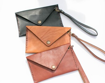 May include: Three leather envelope clutches in black, brown, and reddish-brown with a flap closure and a wrist strap.