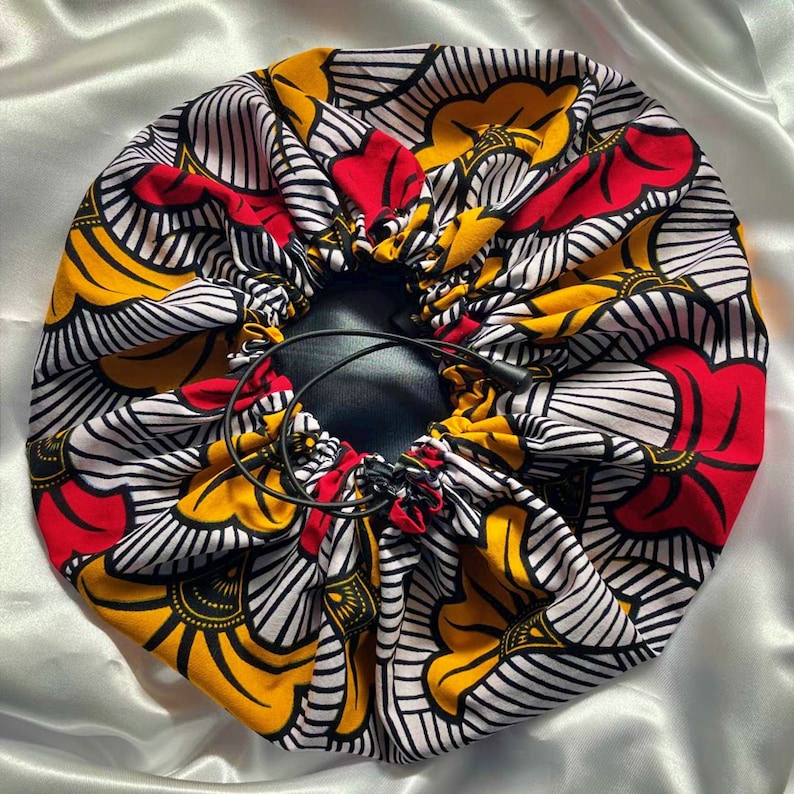 May include: A white, red, and yellow patterned satin bonnet with black drawstring ties. The bonnet is gathered at the top and has a black lining.