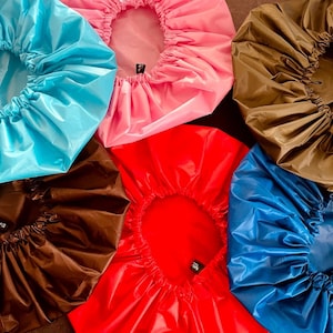 Op de afbeelding: Assortiment van zes douchecaps in verschillende kleuren, waaronder blauw, roze, rood, bruin en zwart. De caps zijn gemaakt van waterdicht materiaal en hebben een geplooide elastische band rond de rand.